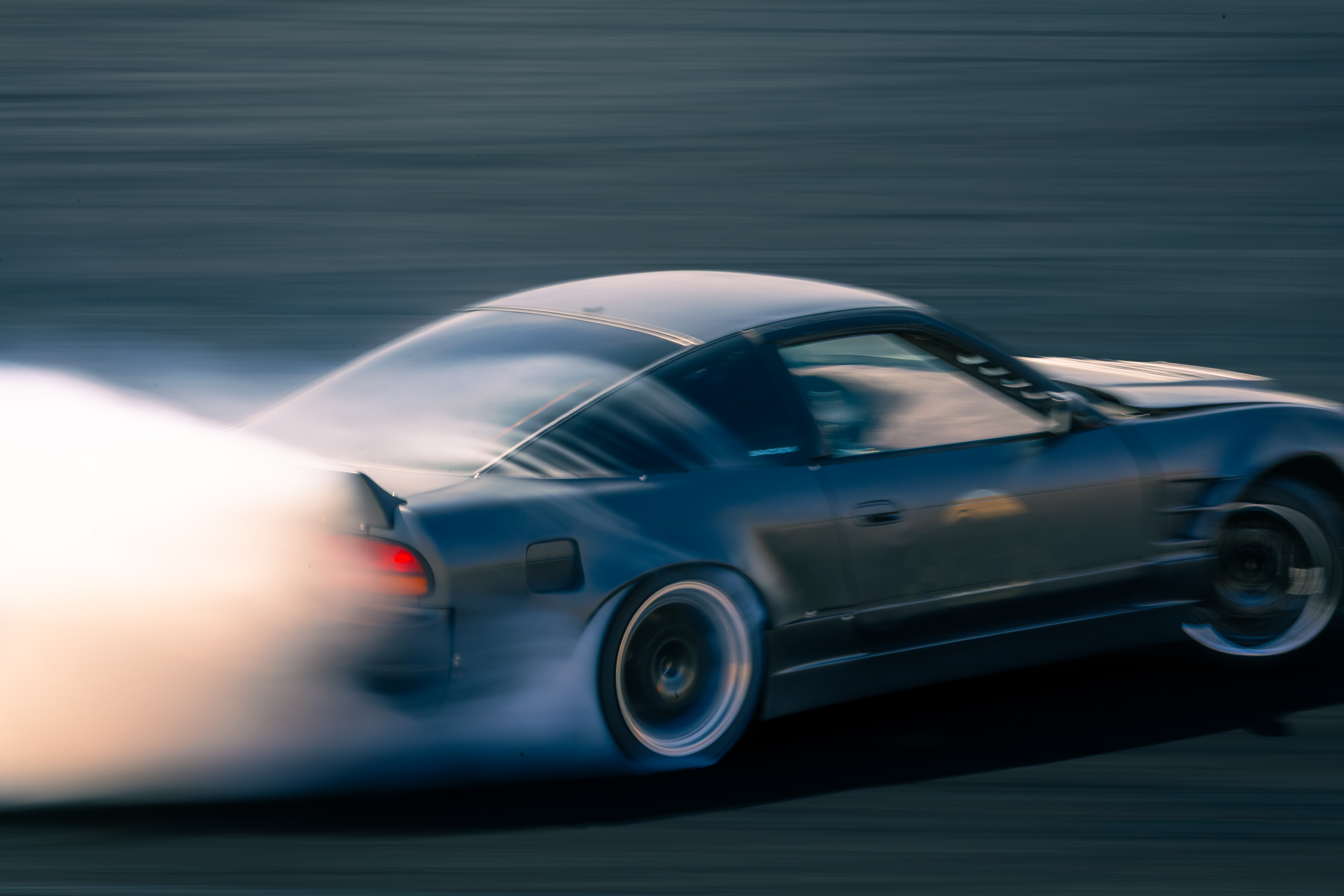 Tire smoke blowing over the trunk of a car as it drifts.